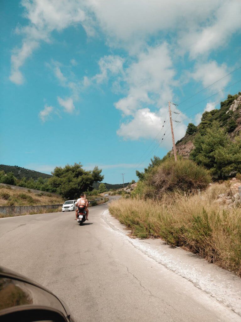 Scenic road in Zakynthos, framed by lush greenery and clear blue skies, embodying the island's natural beauty.